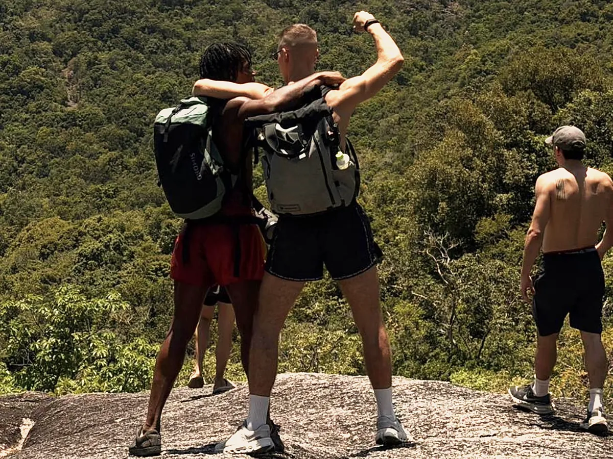 Zwei aus der Gruppe posieren auf einem Felsen, im Hintergrund der bewaldete Berg.